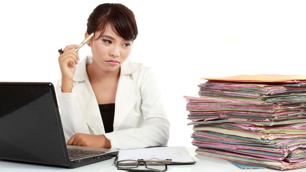Woman contemplates a tall stack of files with a weary look